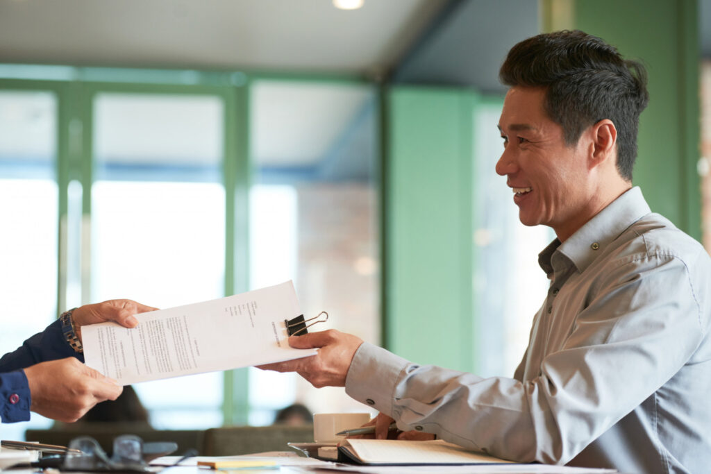 A smiling registered patent agent receiving documents from a client to handle patent prosecution and filings at the Indian Patent Office.