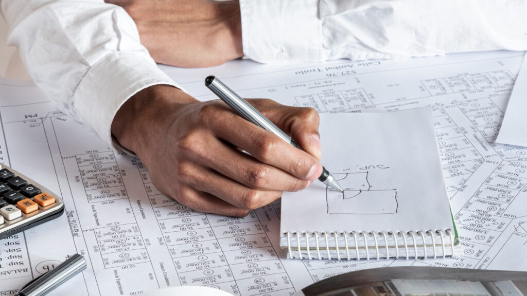 A person's hand sketching an invention on a notepad next to a list of patent drafting elements like Title, Field, and Background.