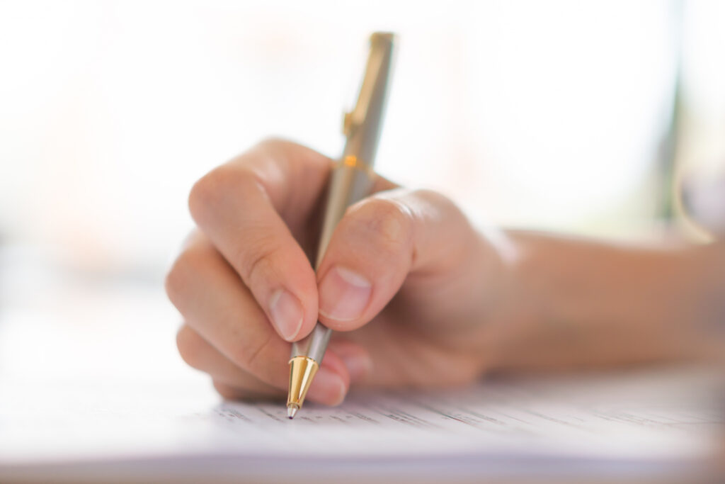 Text explaining how to correct a copyright filing error in India alongside a close-up photo of a hand writing on a document with a silver pen.