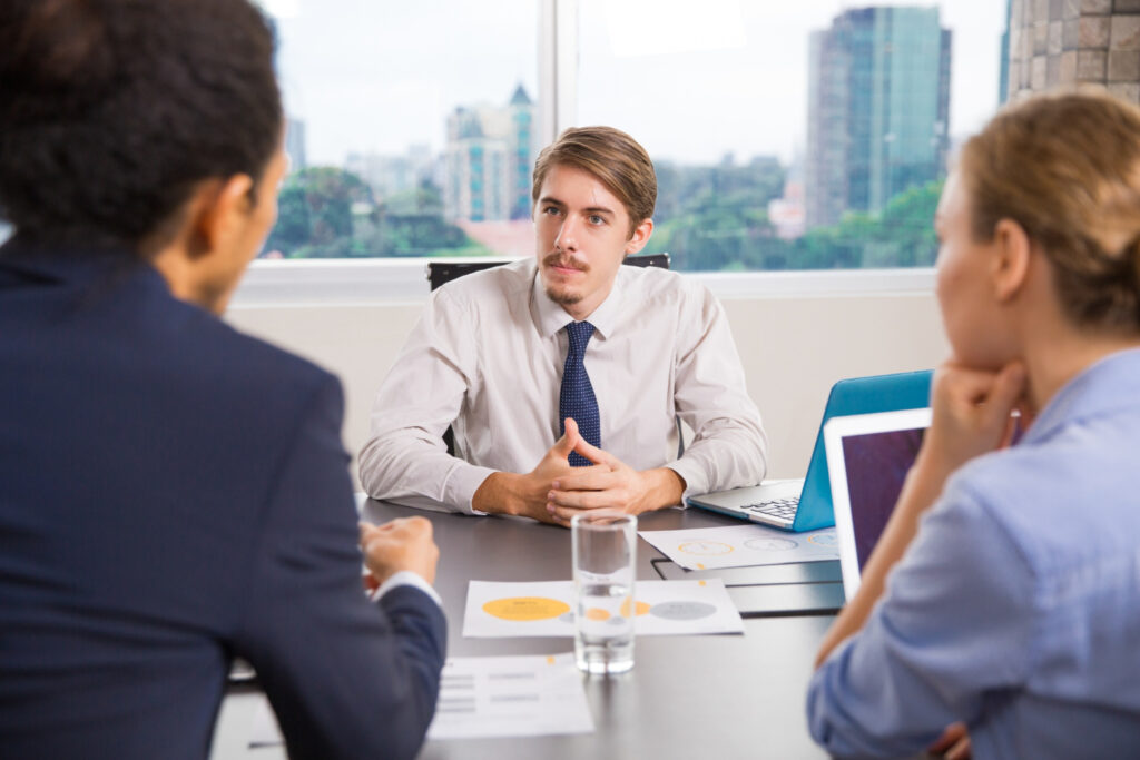 An infographic explaining the hired-to-invent doctrine next to an image of three business professionals discussing employment terms in a corporate office meeting.